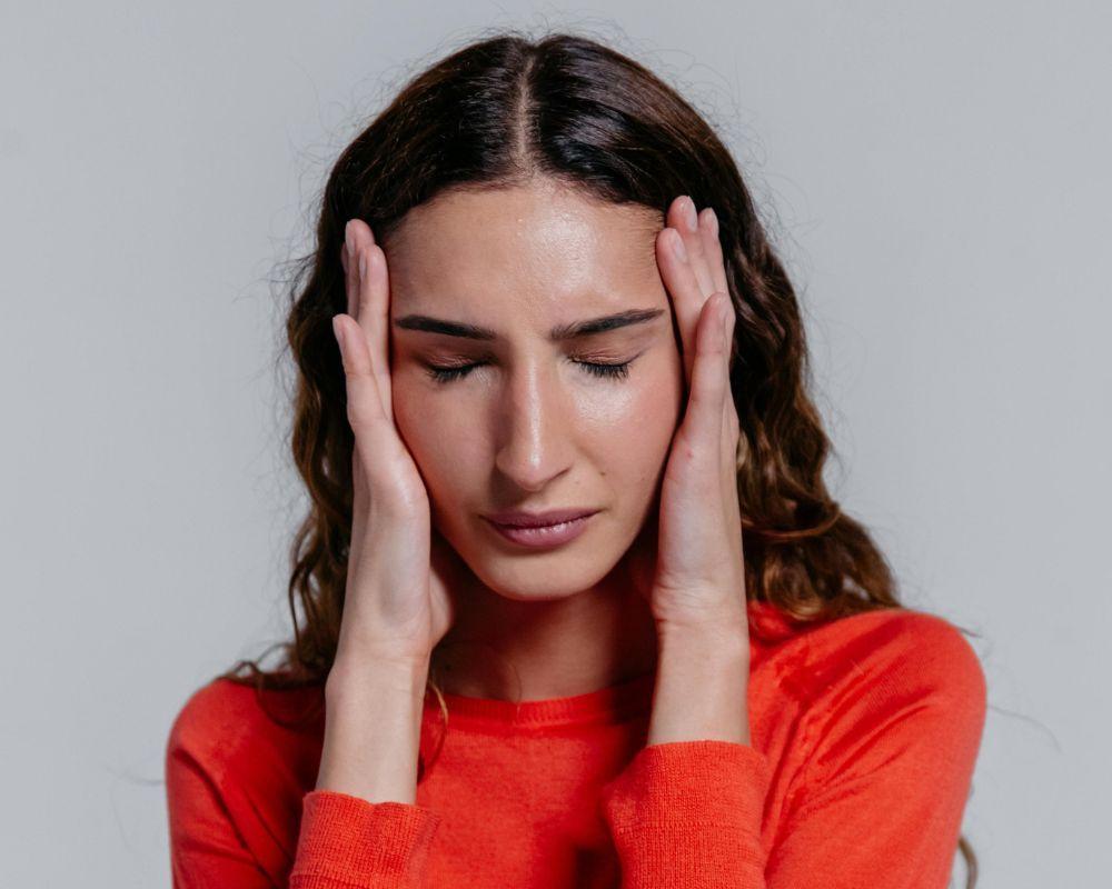 Frau mit Tinnitus in rotem Pullover hält sich mit geschlossenen Augen den Kopf