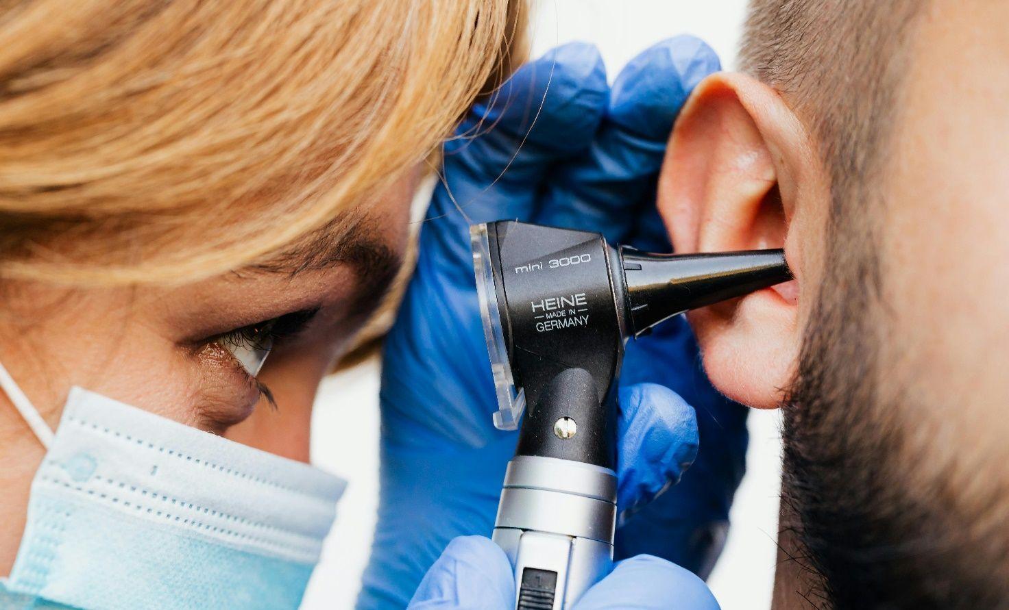 Mann mit Tinnitus wird von einer HNO-Ärztin mit einem Otoskop untersucht