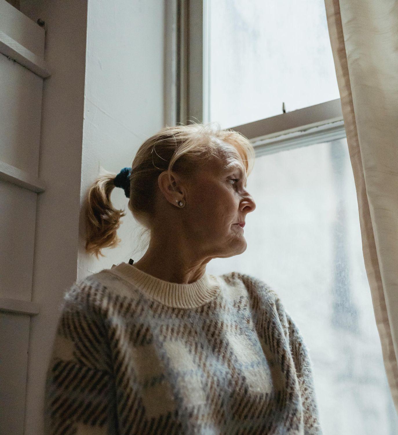 Eine ältere Frau mit Hörproblemen sitzt am Fenster und blickt traurig hinaus.