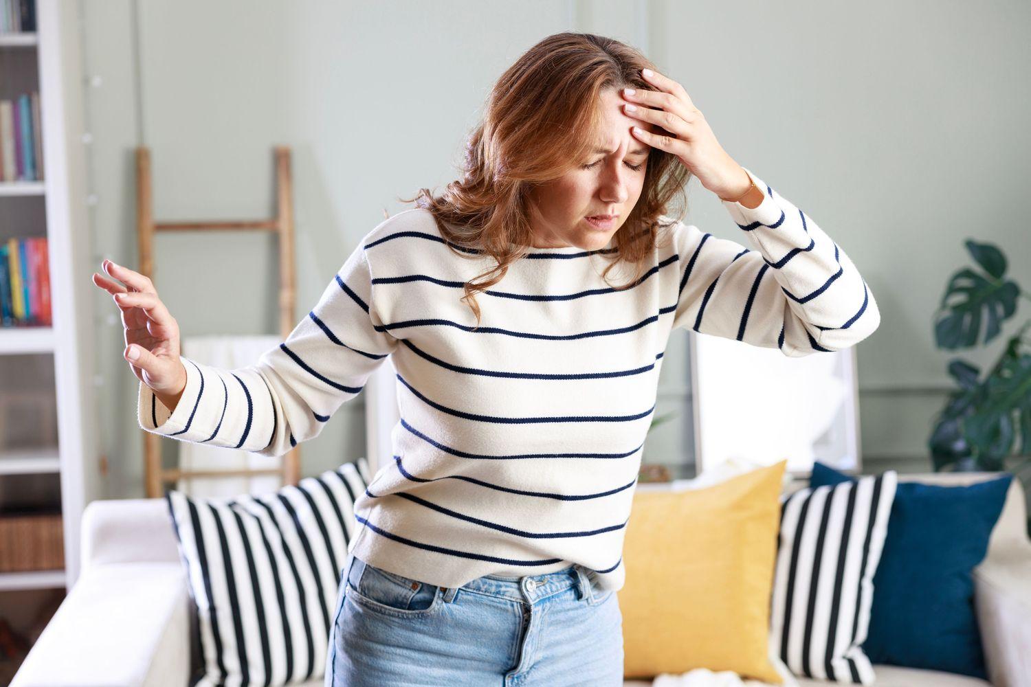 Eine Frau steht in ihrer Wohnung und ihr ist schwindelig, weil ihre Ohren mit Ohrenschmalz verstopft sind.