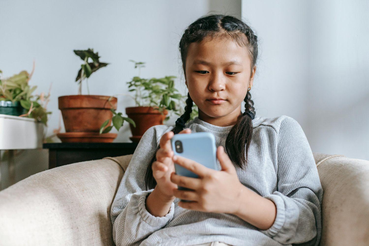 Ein junges Mädchen in einem grauen Pullover sitzt auf dem Sofa und absolviert auf ihrem Smartphone ein Hörtraining.