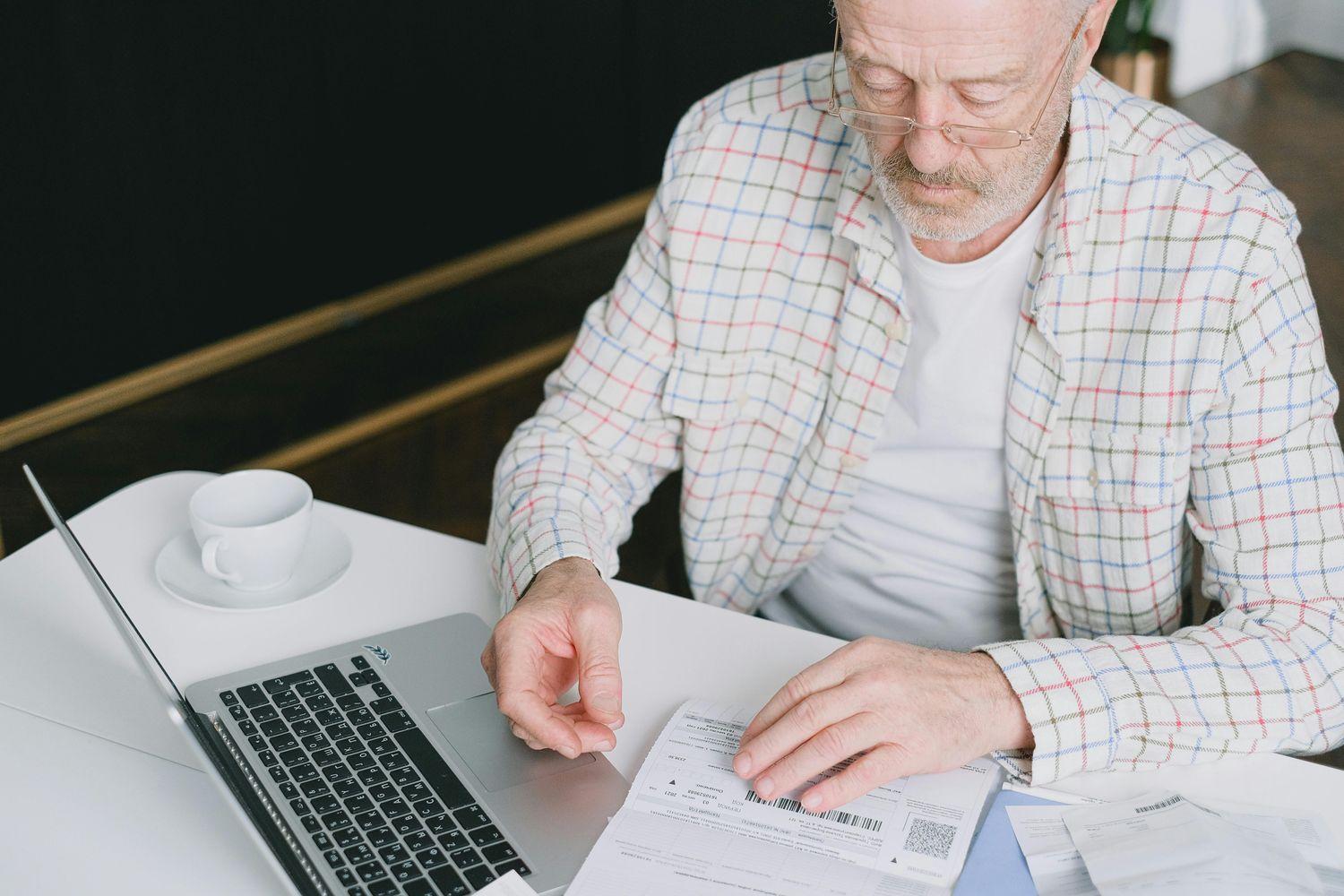 Ein älterer Mann sitzt vor dem Laptop mit Dokumenten