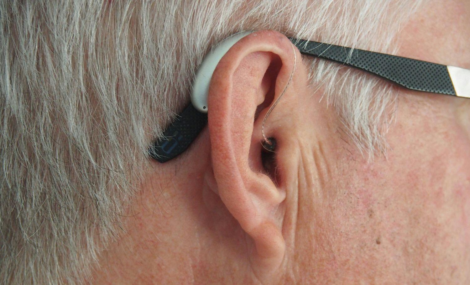 Seitliche Nahaufnahme eines älteren Mannes mit grauen Haaren und einer Brille, der ein Hörgerät trägt.