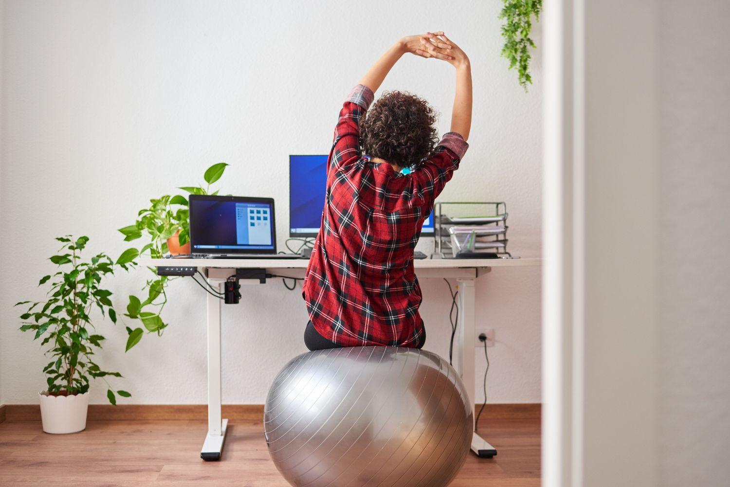 Ein Mann sitzt während eines Online-Meetings auf einem Gymnastikball und dehnt sich
