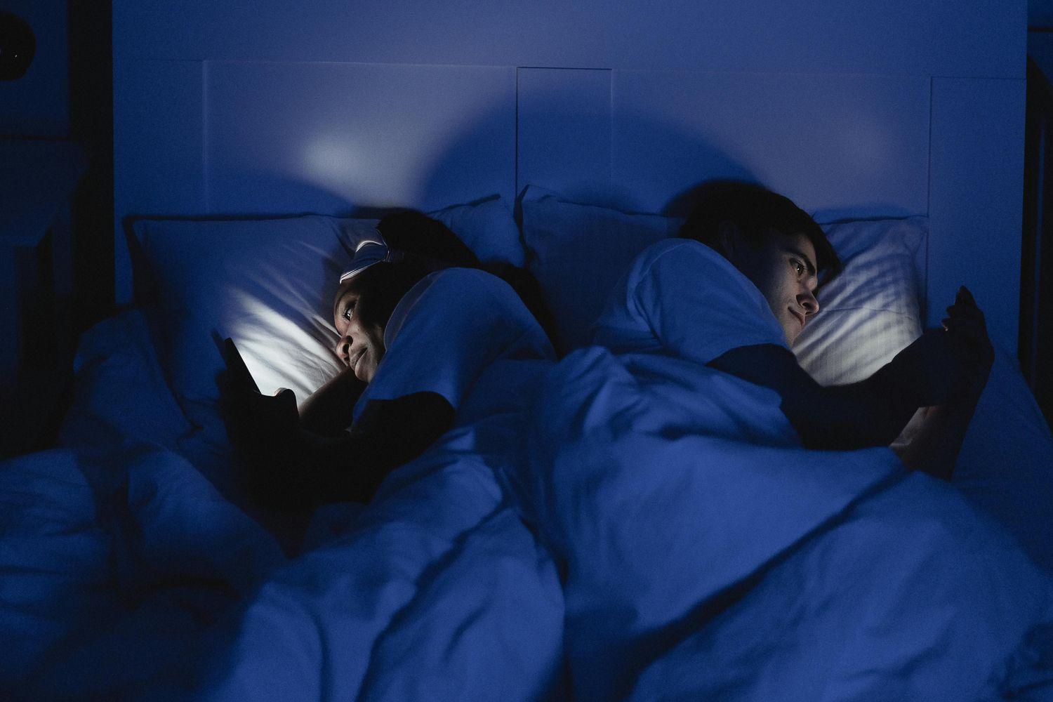 Ein Paar liegt im Bett, wobei sich beide den Rücken zuwenden und auf ihre Smartphones schauen